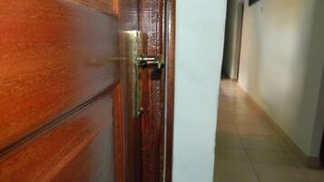 A wooden door with a brass handle and a keyhole, leading into a hallway with a tiled floor and white walls.