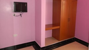 A room with pink walls, a wooden wardrobe, a small shelf, and a mounted television.