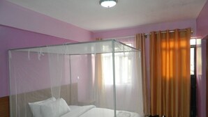A room with a bed covered by a mosquito net, a nightstand, and a window with curtains.