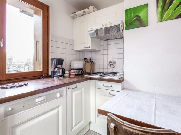 Una cocina con armarios blancos, estufa, cafetera y ventana.