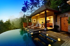 A luxurious outdoor pool area with lounge chairs, a wooden deck, and a well-lit interior space with a dining area. - Kenran Resort Ubud by Soscomma (Ubud)