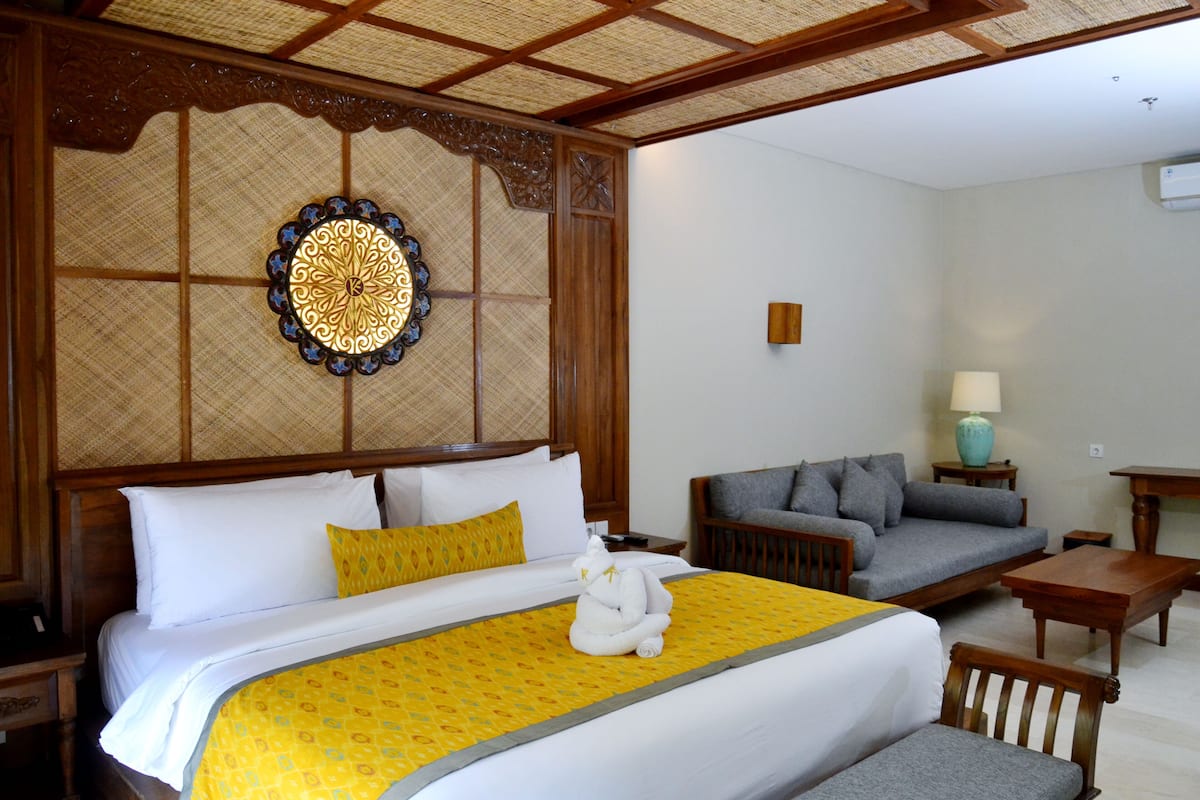 A hotel room with a large bed, a sofa, a small table, and a decorative wall piece.