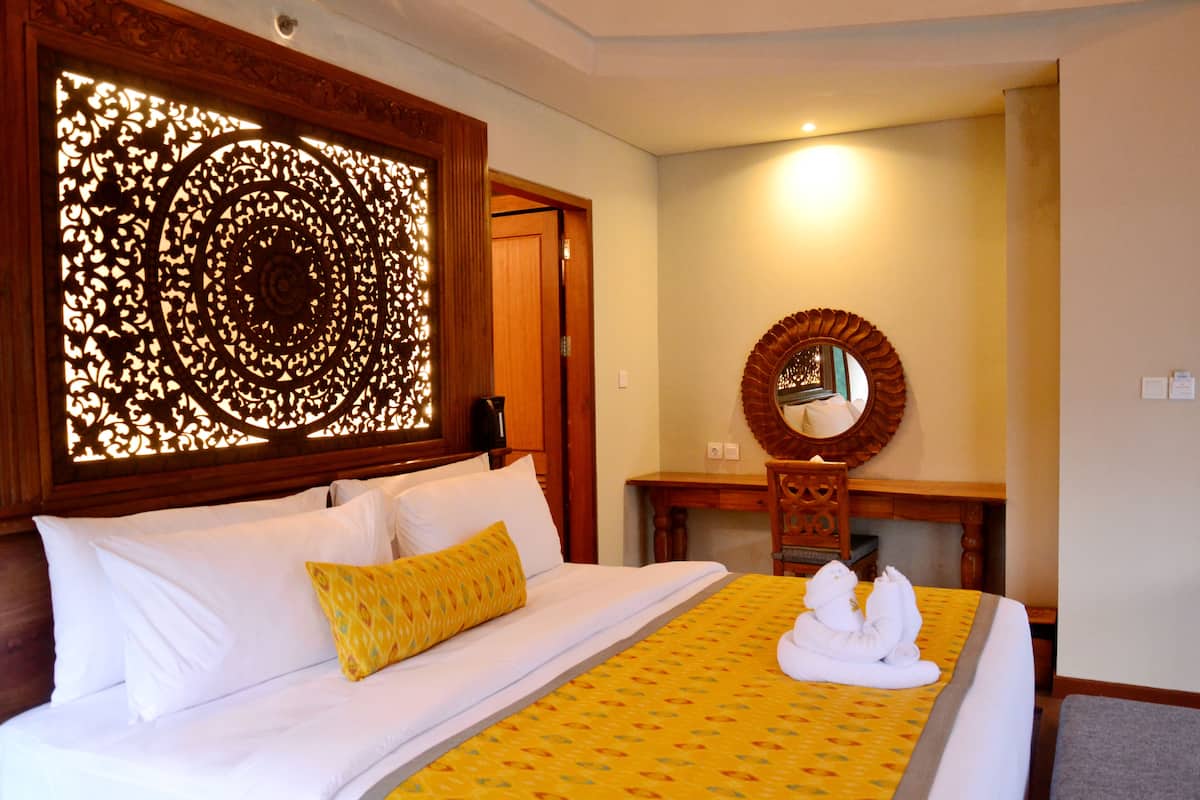 A hotel room with a bed, a wooden headboard, a desk with a mirror, and a decorative screen.