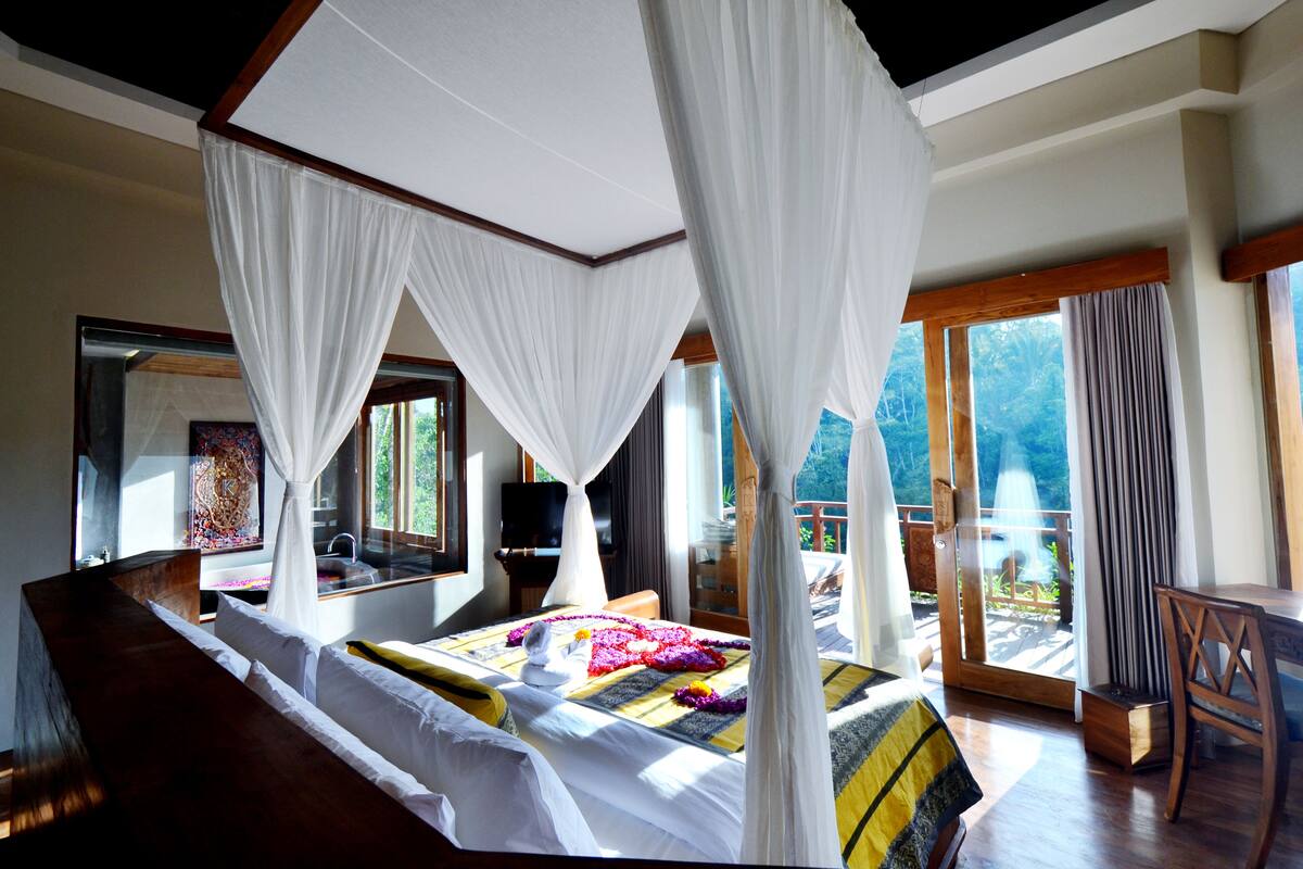 A bedroom with a four-poster bed, a large window, and a balcony.