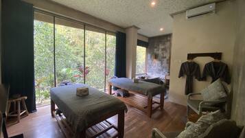 Relax in a serene space with a view of lush greenery, featuring two massage tables and a stone wall.