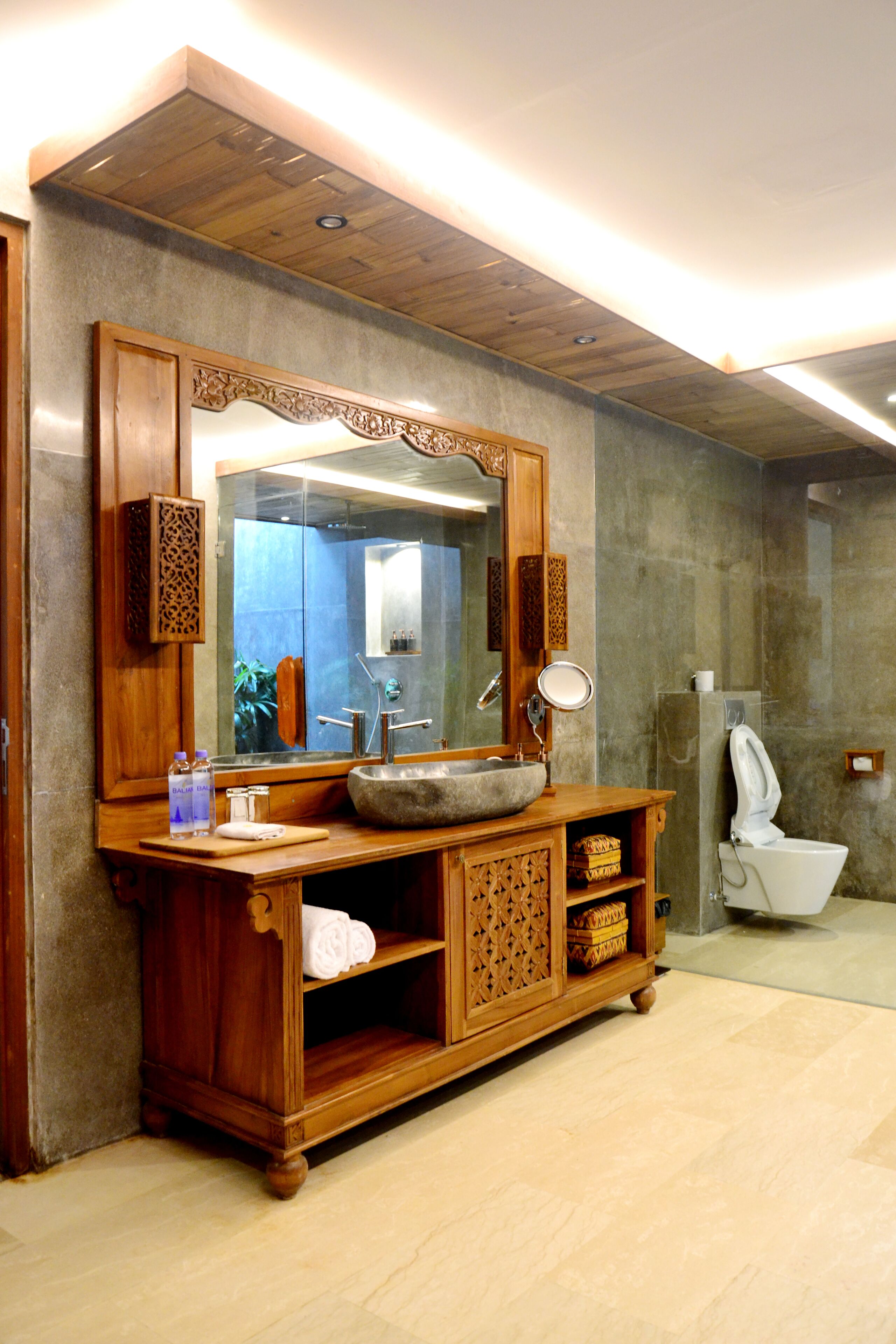 A bathroom with a wooden vanity, a large mirror, a sink, and a toilet.