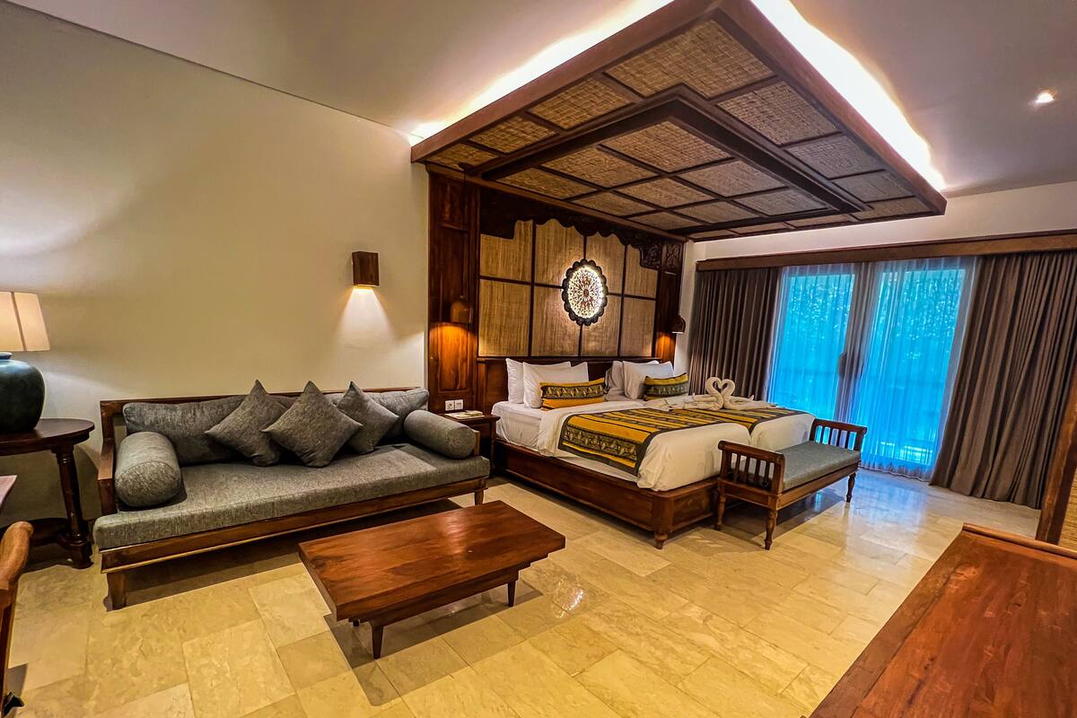 A hotel room with a sofa, a wooden bed, a wooden coffee table, and a wooden chair.