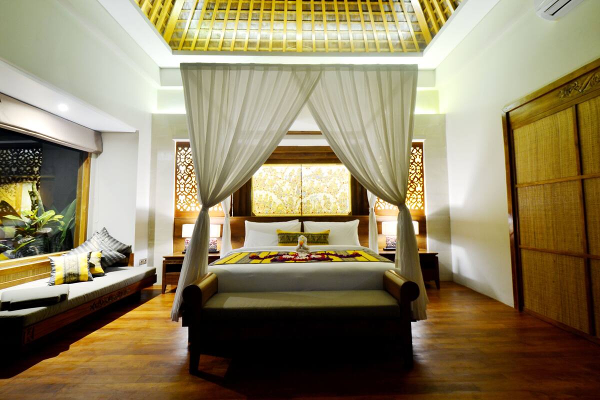 A room with a bed under a canopy, a sofa, and a wooden floor.