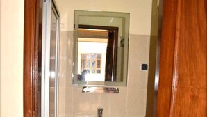 A small bathroom with a white sink, a mirror above it, and a shower door. - Hôtel Kin Comfort (Kinshasa)
