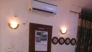 A room with a wooden door, a bulletin board, a wall-mounted air conditioner, and a red chair. - Hôtel Kin Comfort (Kinshasa)