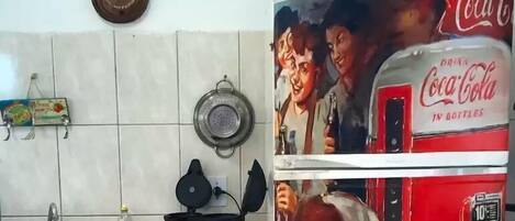 Cozinha com fogão, panelas, pia e geladeira com propaganda de Coca-Cola.