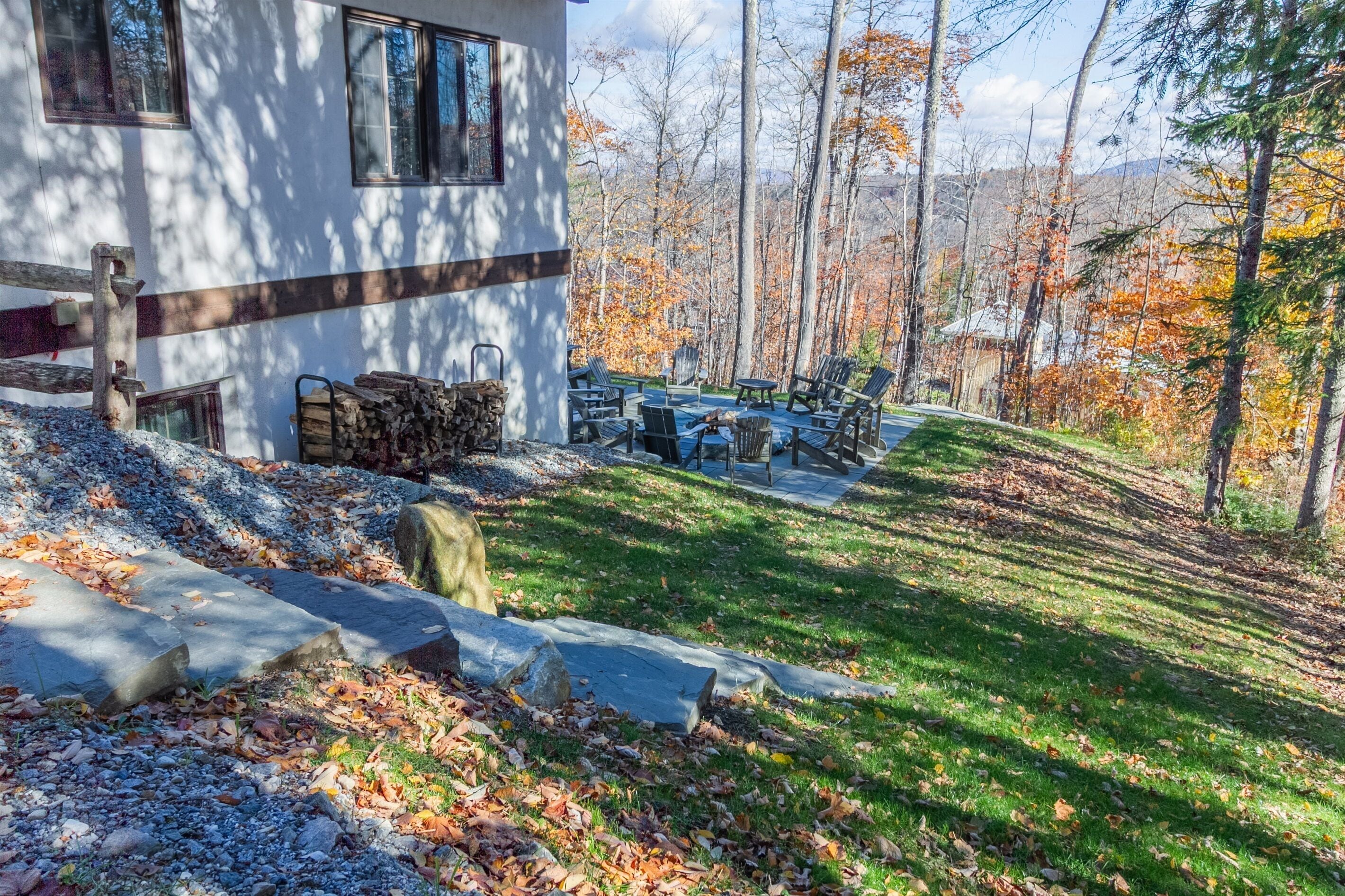 A house with a patio area, stone steps, and a view of a forest with autumn leaves.