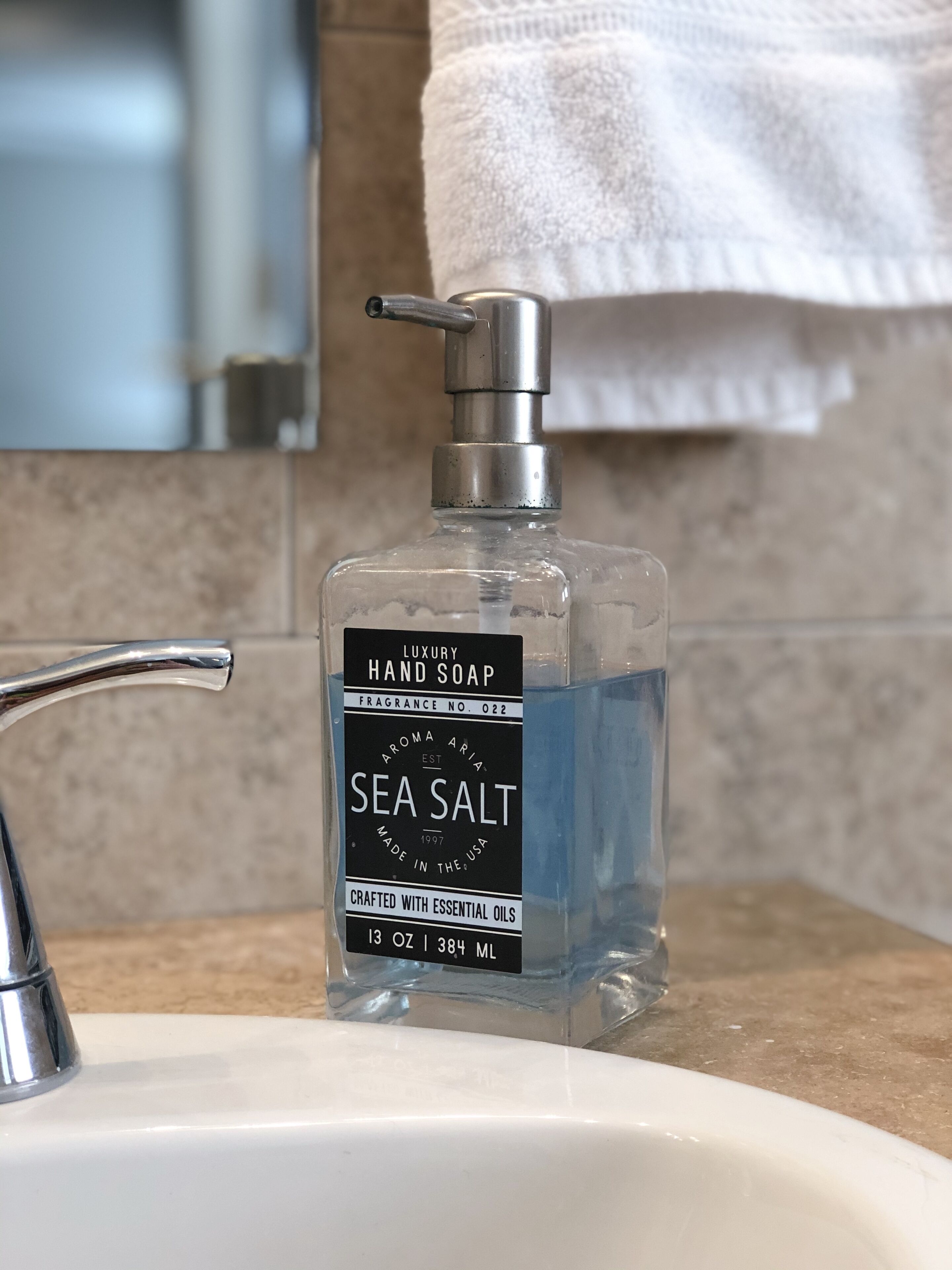 Un lavandino in bagno con una bottiglia di sapone per le mani etichettata 'Sea Salt' e un rubinetto d'argento.
