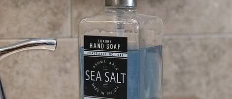 Un lavamanos de baño con una botella de jabón de manos etiquetada como "Sea Salt" y un grifo plateado.