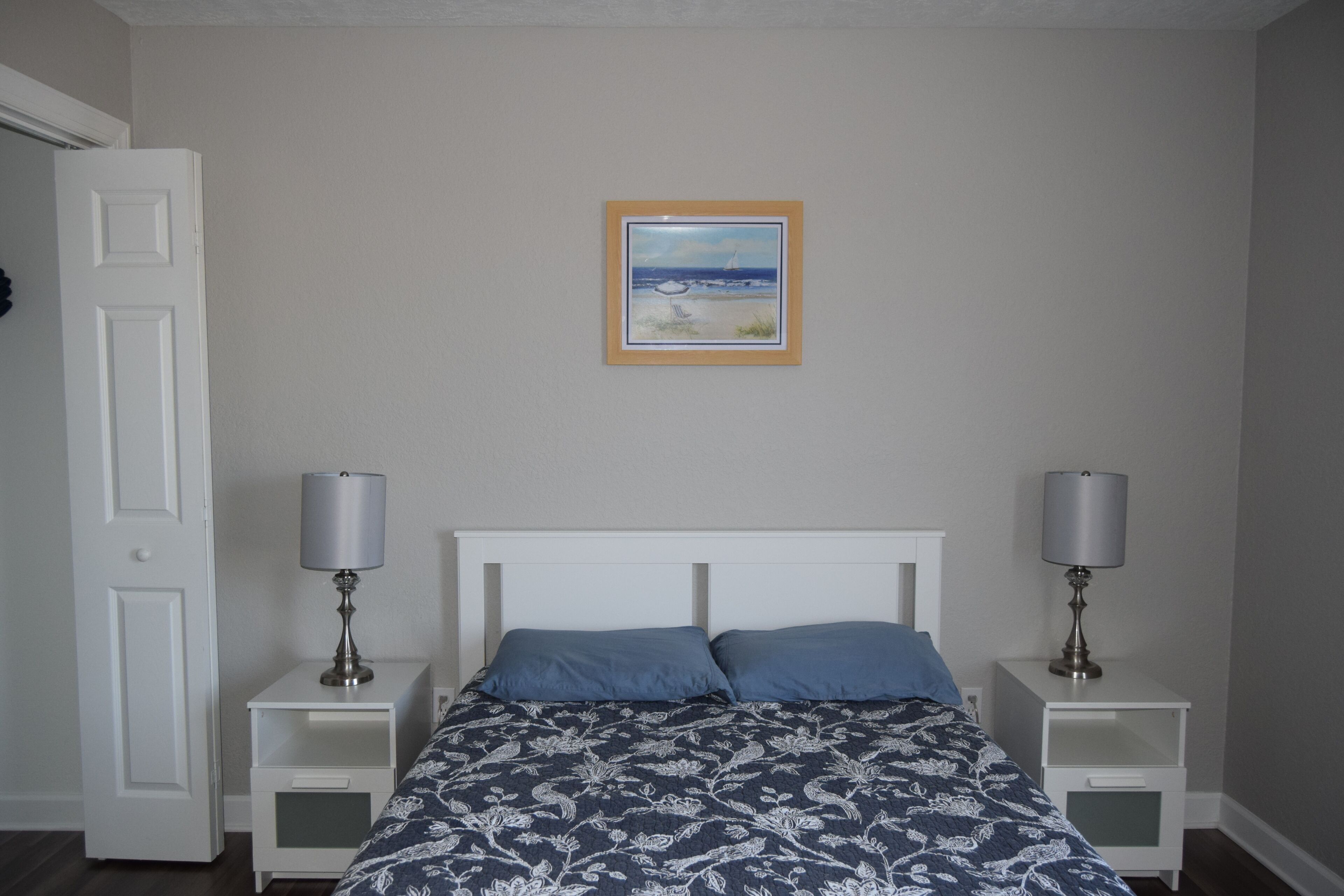 Een slaapkamer met een bed, twee nachtkastjes met lampen, een ingelijste foto aan de muur en een deur.