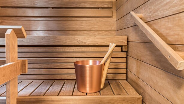 A wooden sauna bench with a copper bucket and wooden ladle.