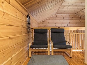 Een houten interieur met twee gestoffeerde fauteuils en een bankje, een decoratie aan de muur, en een houten vloer.
