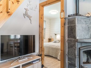 Un intérieur moderne avec une télévision, des meubles en bois, une cheminée et un lit recouvert d’une couverture matelassée.