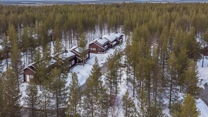 A row of log cabins in a forest with snow-covered ground.