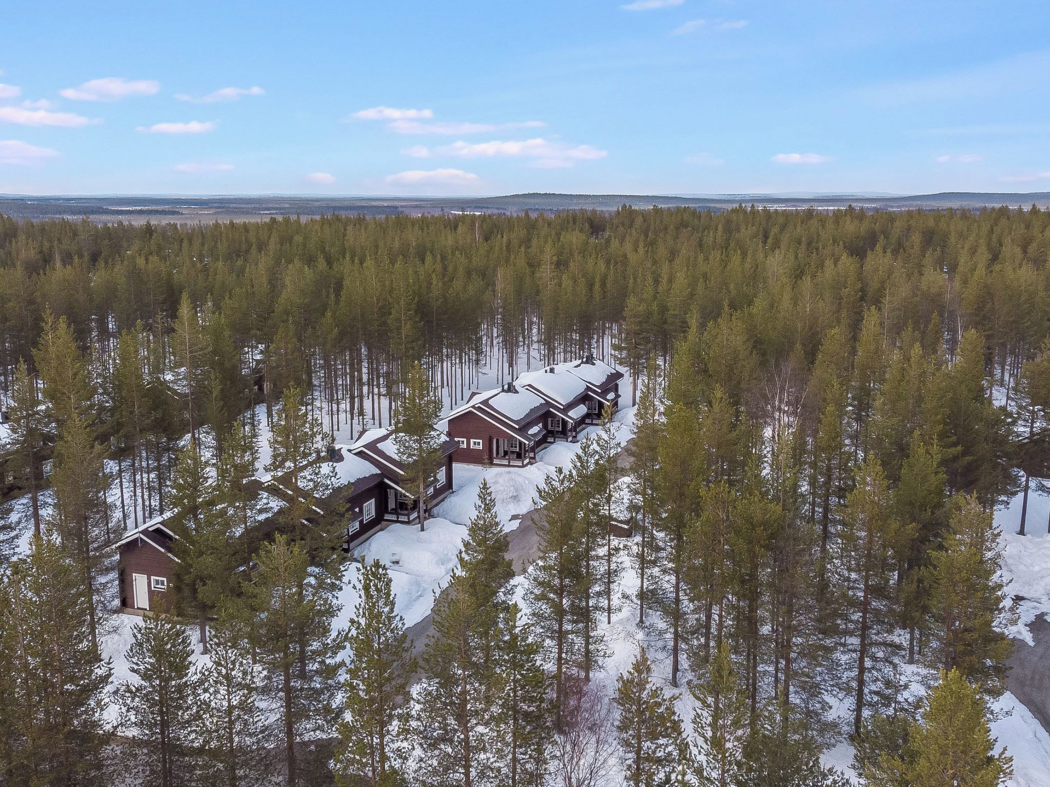 Een rij vakantiehuisjes in een besneeuwd bos onder een heldere lucht.