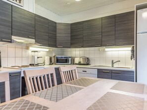 Een moderne keuken met donkere houten kastjes, een roestvrijstalen spoelbak en een eethoek met een tafel en stoelen.