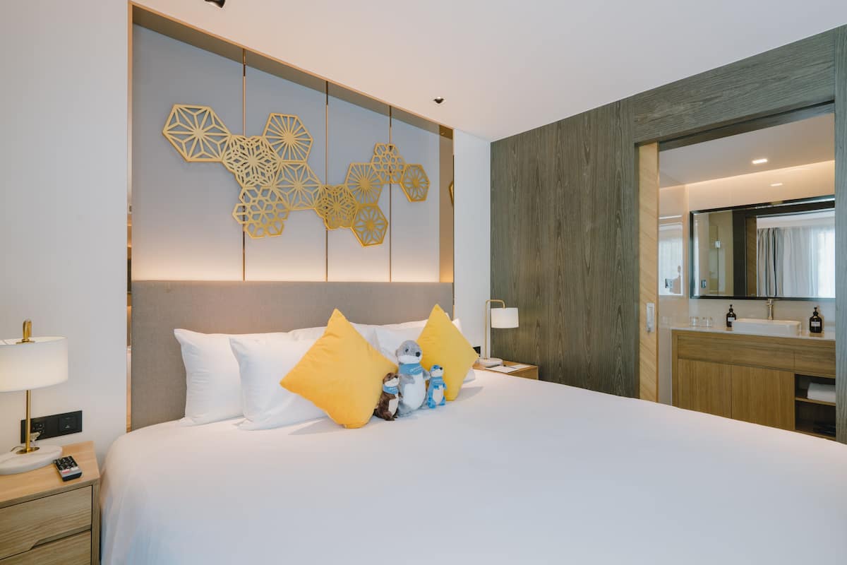 Een moderne hotelkamer met een groot bed, een houten hoofdbord, een geometrisch wandlamp en een houten kaptafel met spiegel.