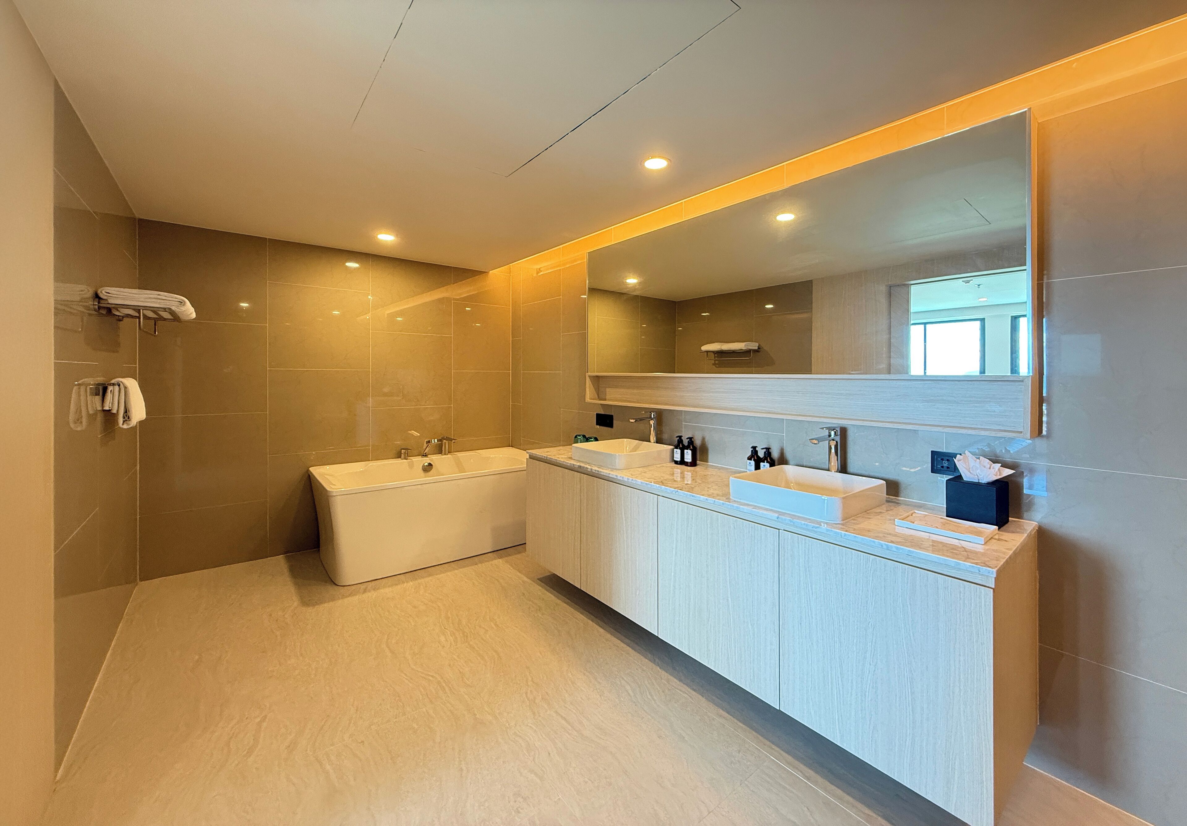 A modern bathroom with a bathtub, two sinks, and a large mirror.