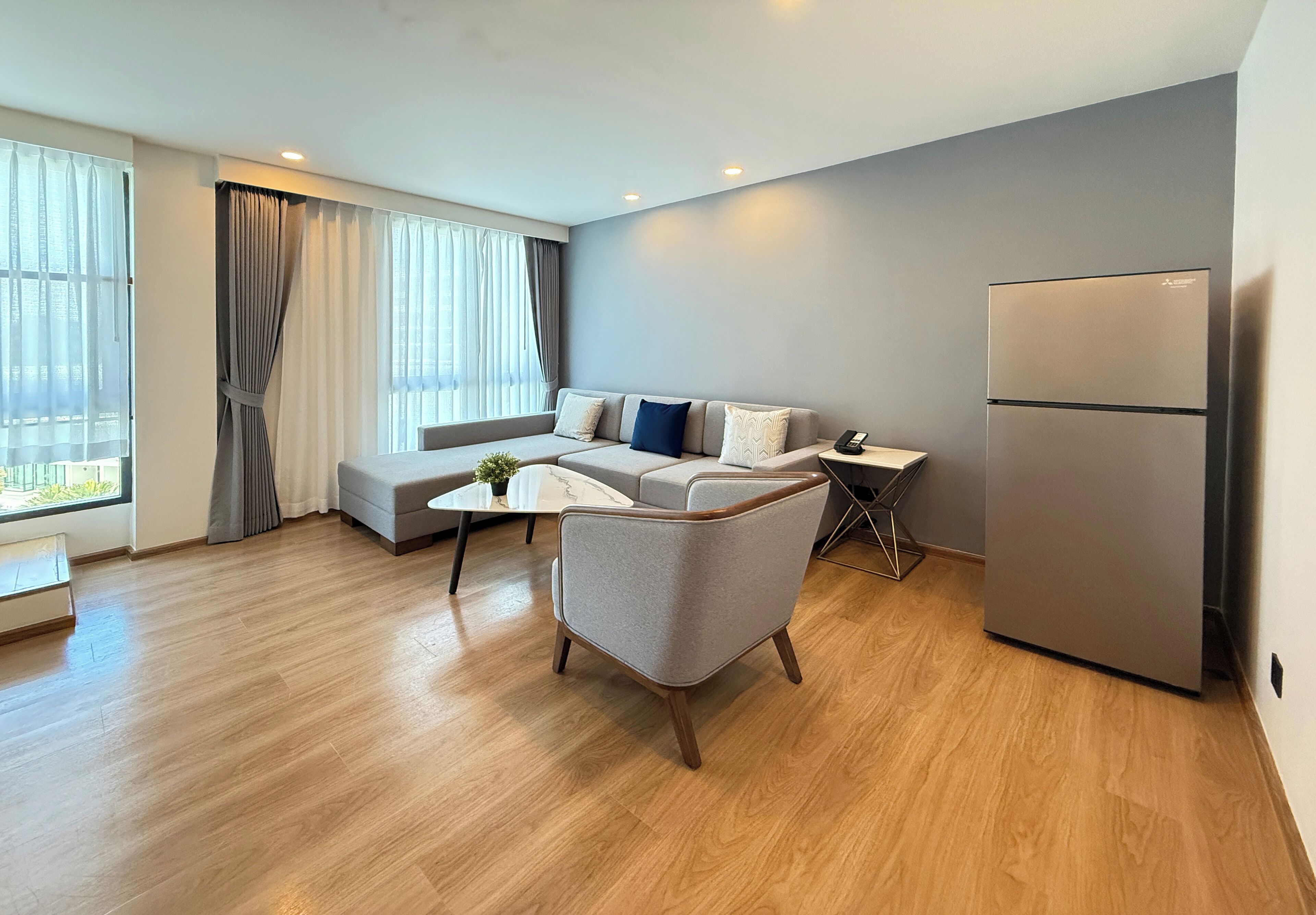Una sala de estar moderna con un sofá, una mesa de centro y una mesa de comedor. Hay un refrigerador y una ventana con cortinas.
