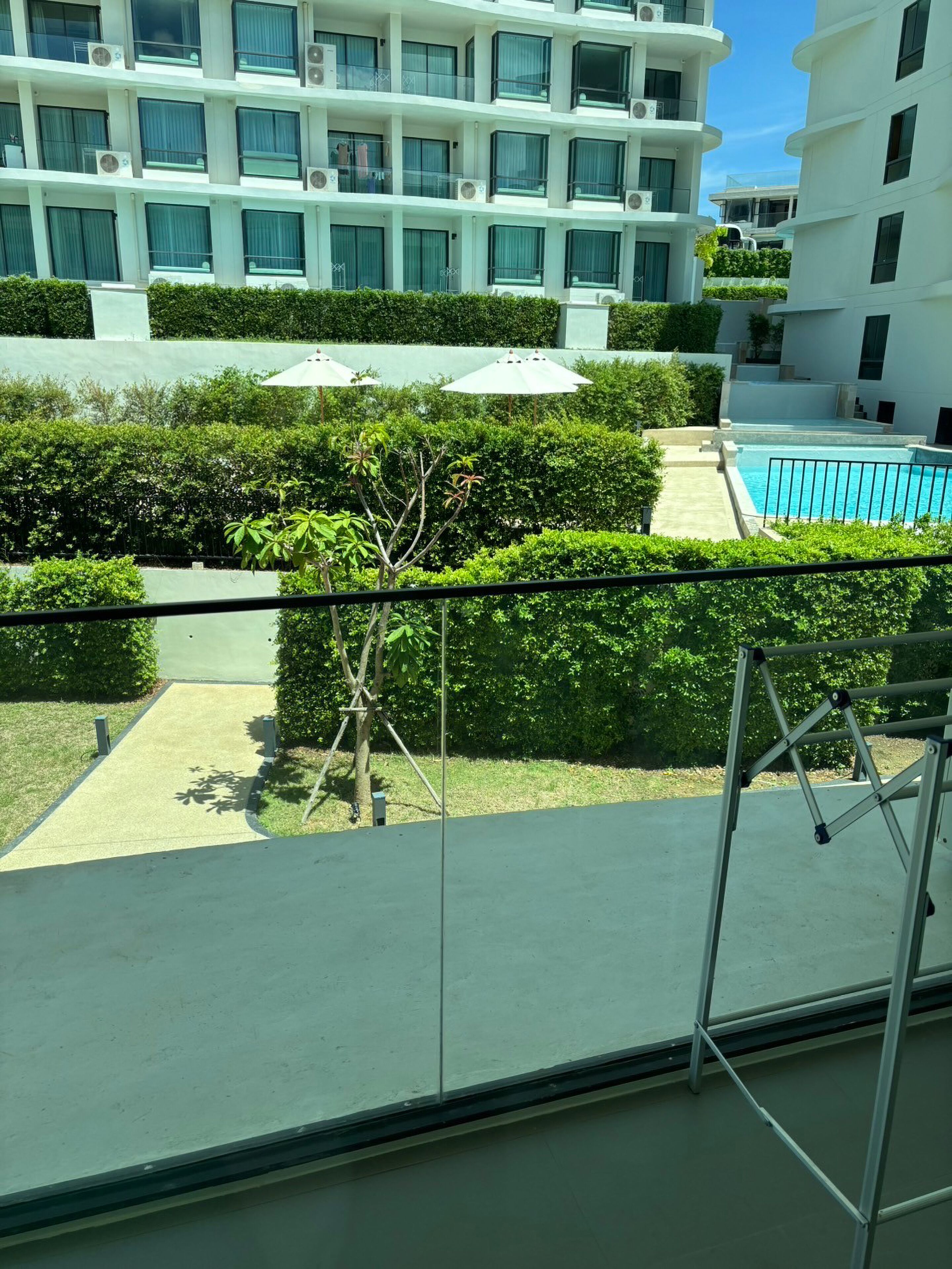Un edificio moderno con varios balcones, piscina y abundante vegetación.