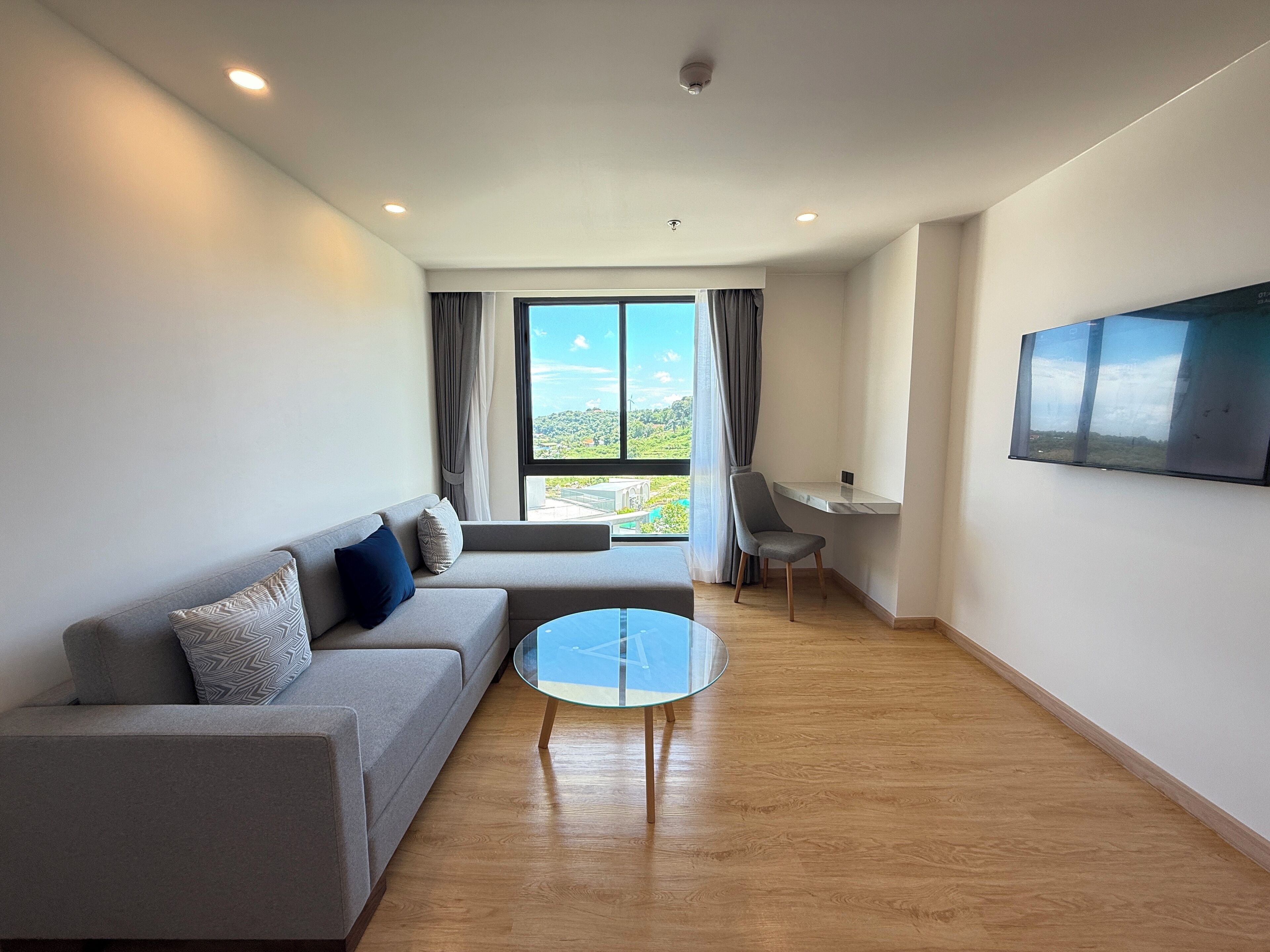 A modern living room with a grey sofa, a glass coffee table, and a TV mounted on the wall.