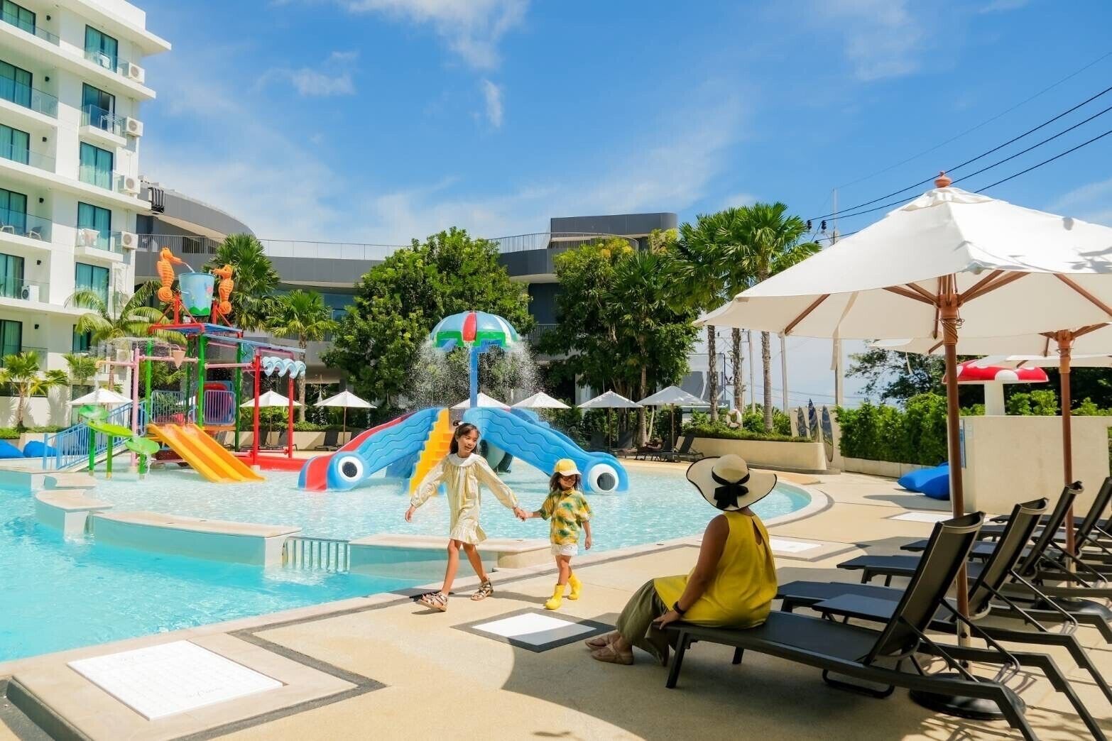 A swimming pool area with a water play structure, lounge chairs, and umbrellas.