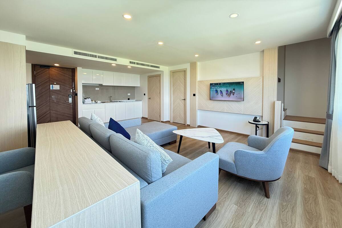 Een moderne woonkamer met een bank, fauteuils, een salontafel en een aan de muur bevestigde televisie.