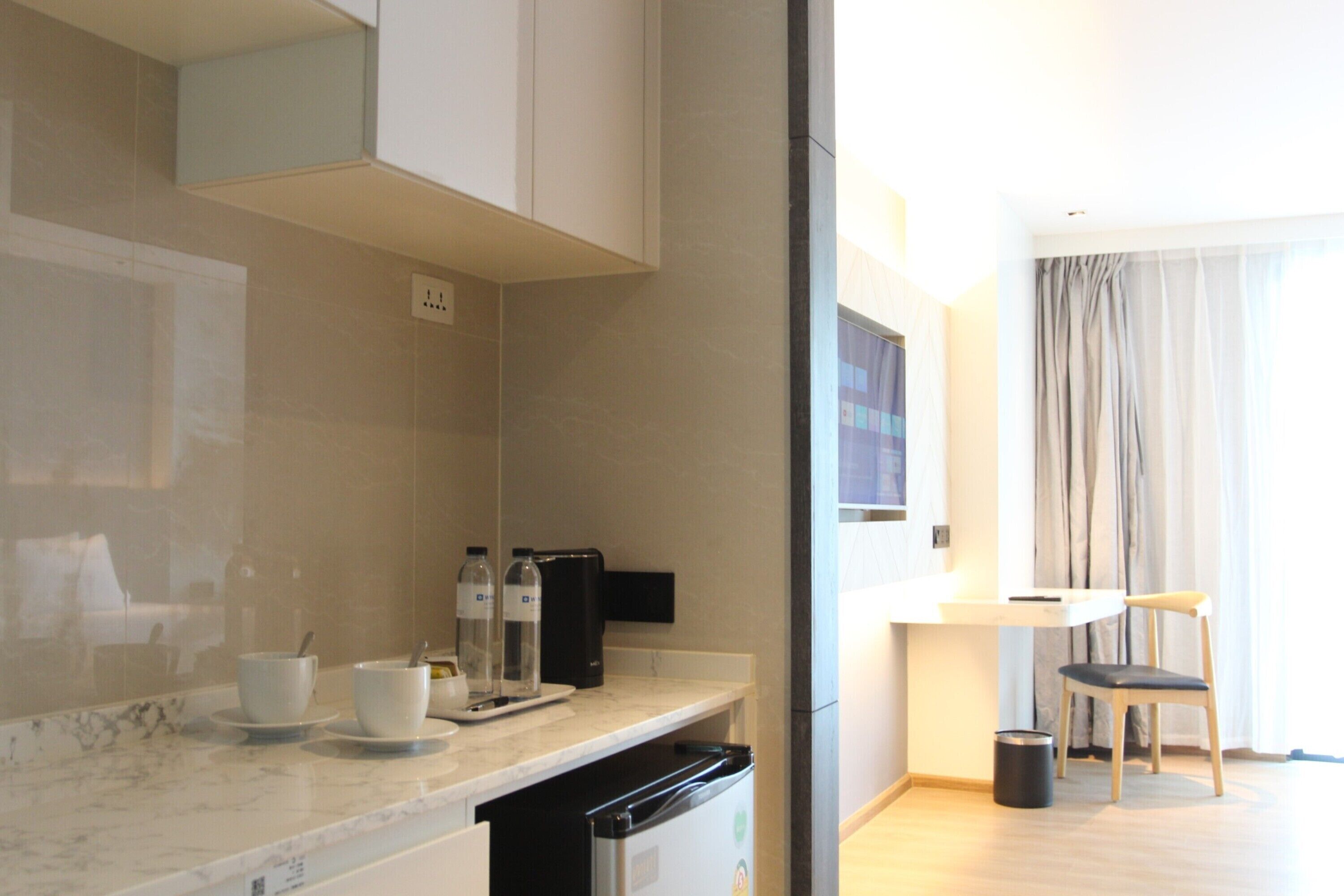 A modern kitchen with a marble countertop, a coffee machine, and a small refrigerator. There is a dining area with a table and chairs visible through an open door.