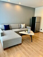 Una sala de estar moderna con un sofá seccional gris, una mesita de centro redonda y un refrigerador negro.