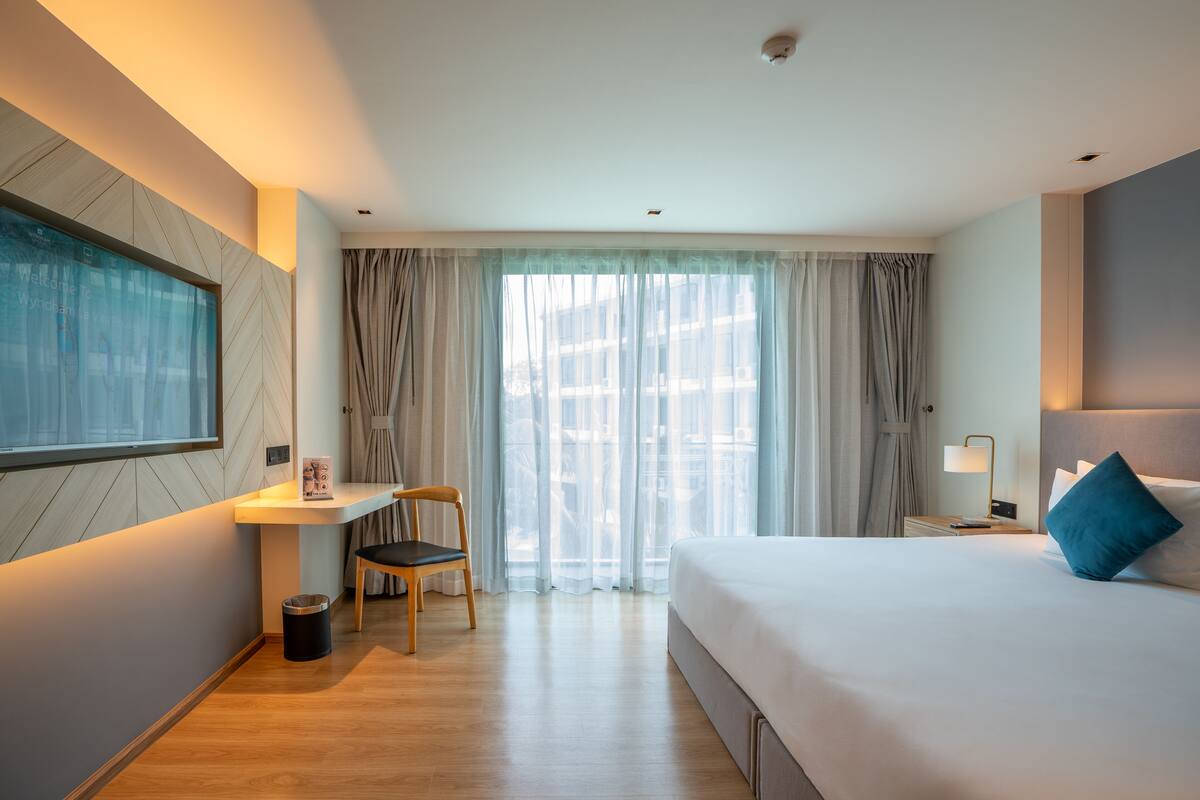 Een hotelkamer met een bed, een bureau, een stoel, een raam met gordijnen en een wandgemonteerde televisie.