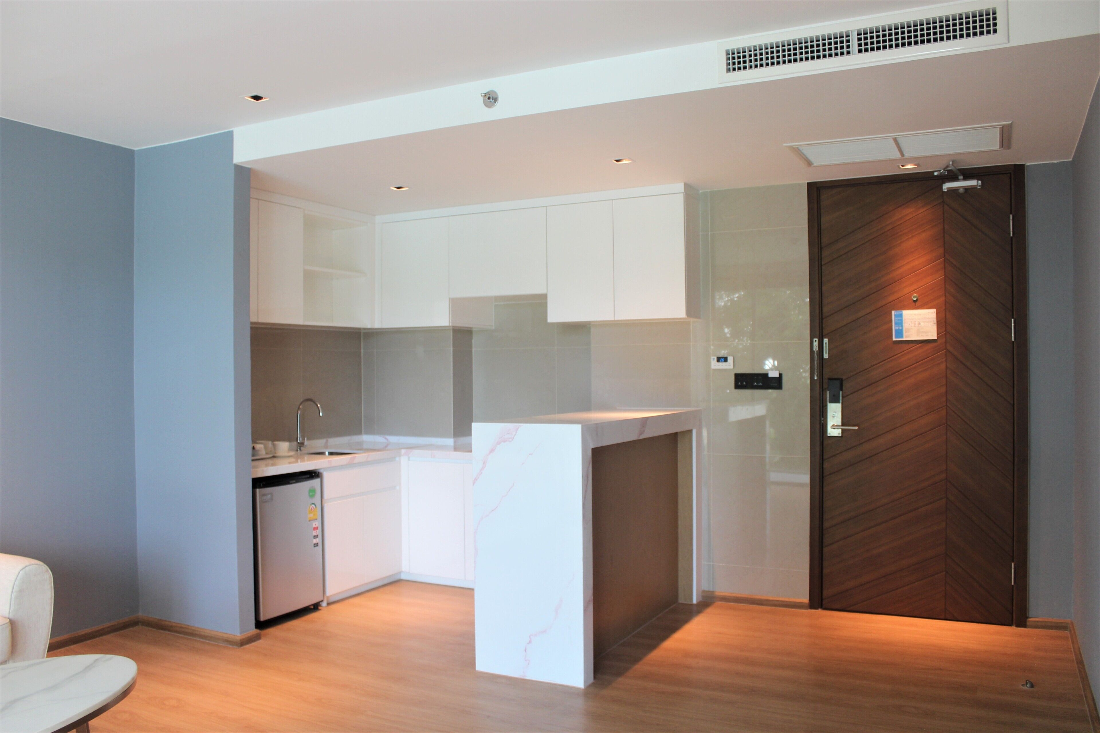 A modern kitchen with white cabinets, a marble countertop, and a wooden door.