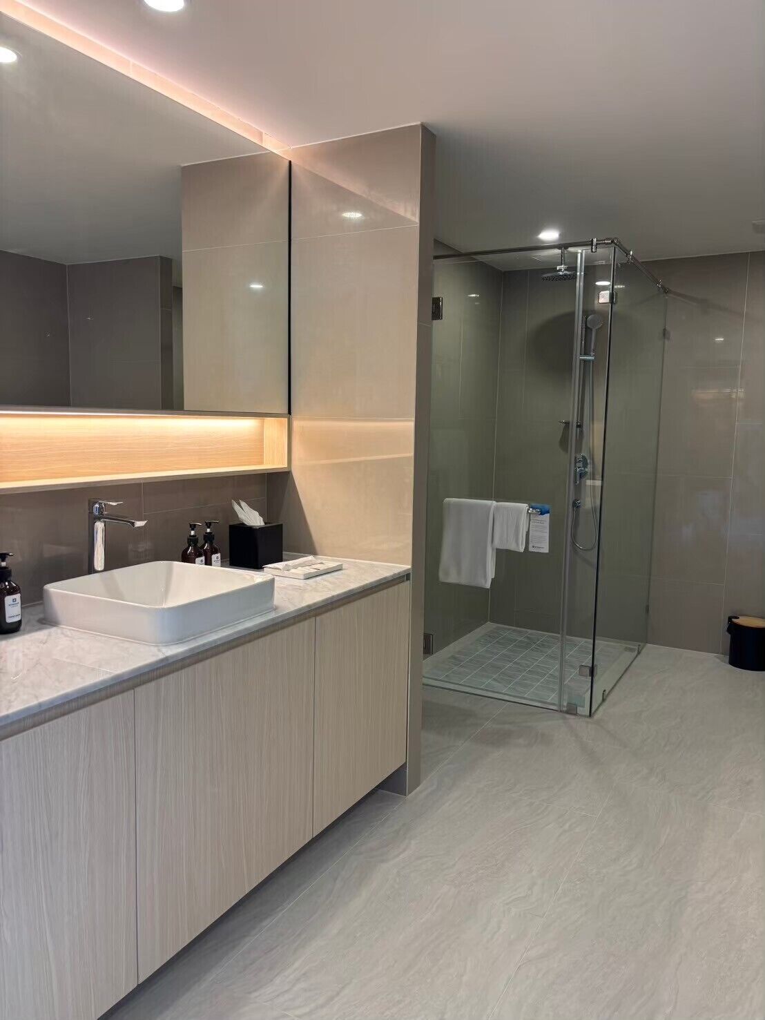 Un baño moderno con un espejo grande, un lavabo blanco y una ducha con cerramiento de vidrio.