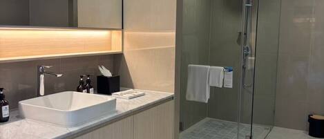 Un baño moderno con un espejo grande, un lavabo blanco y una ducha con cerramiento de vidrio.