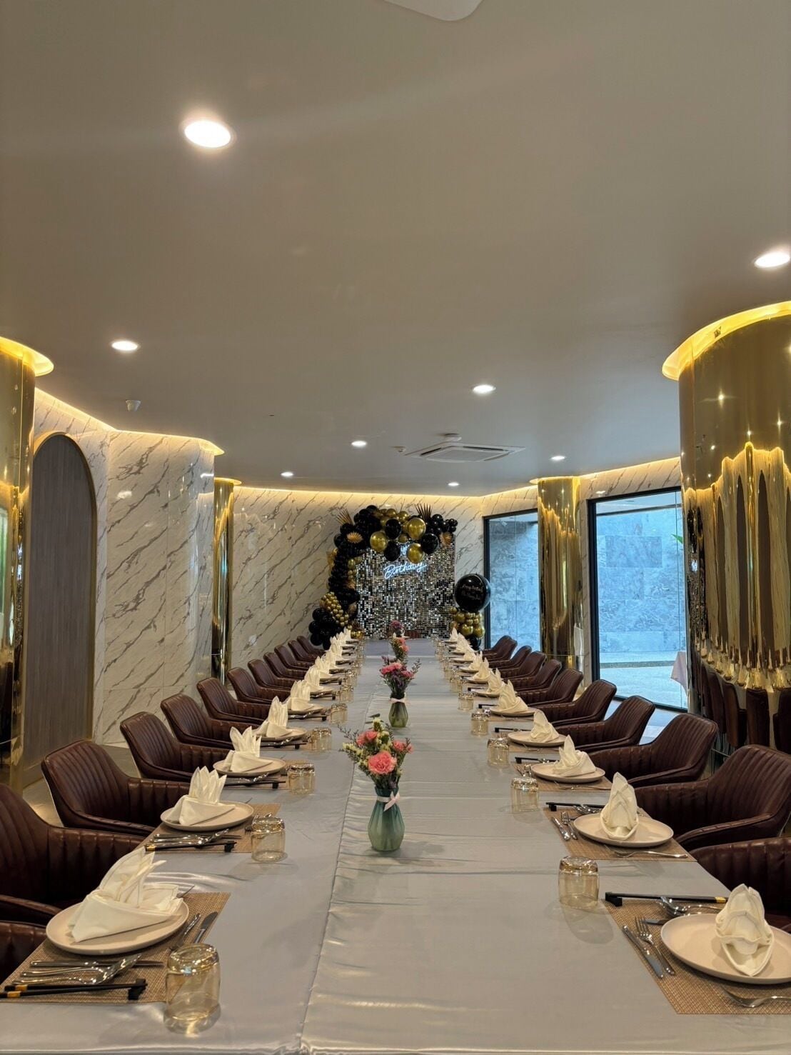 A long conference table with leather chairs, a marble wall, and a chandelier.