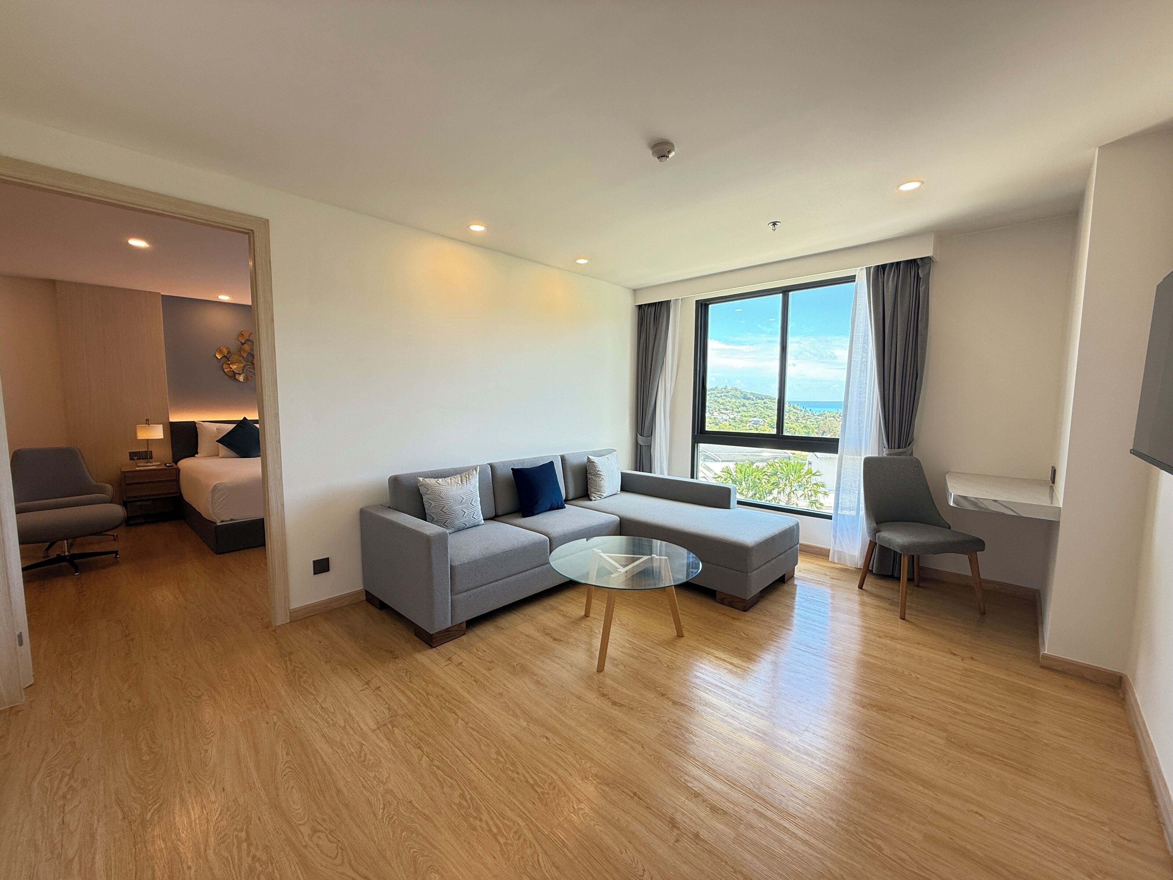 A modern living room with a grey sofa, a round coffee table, and a view of the outdoors through large windows.
