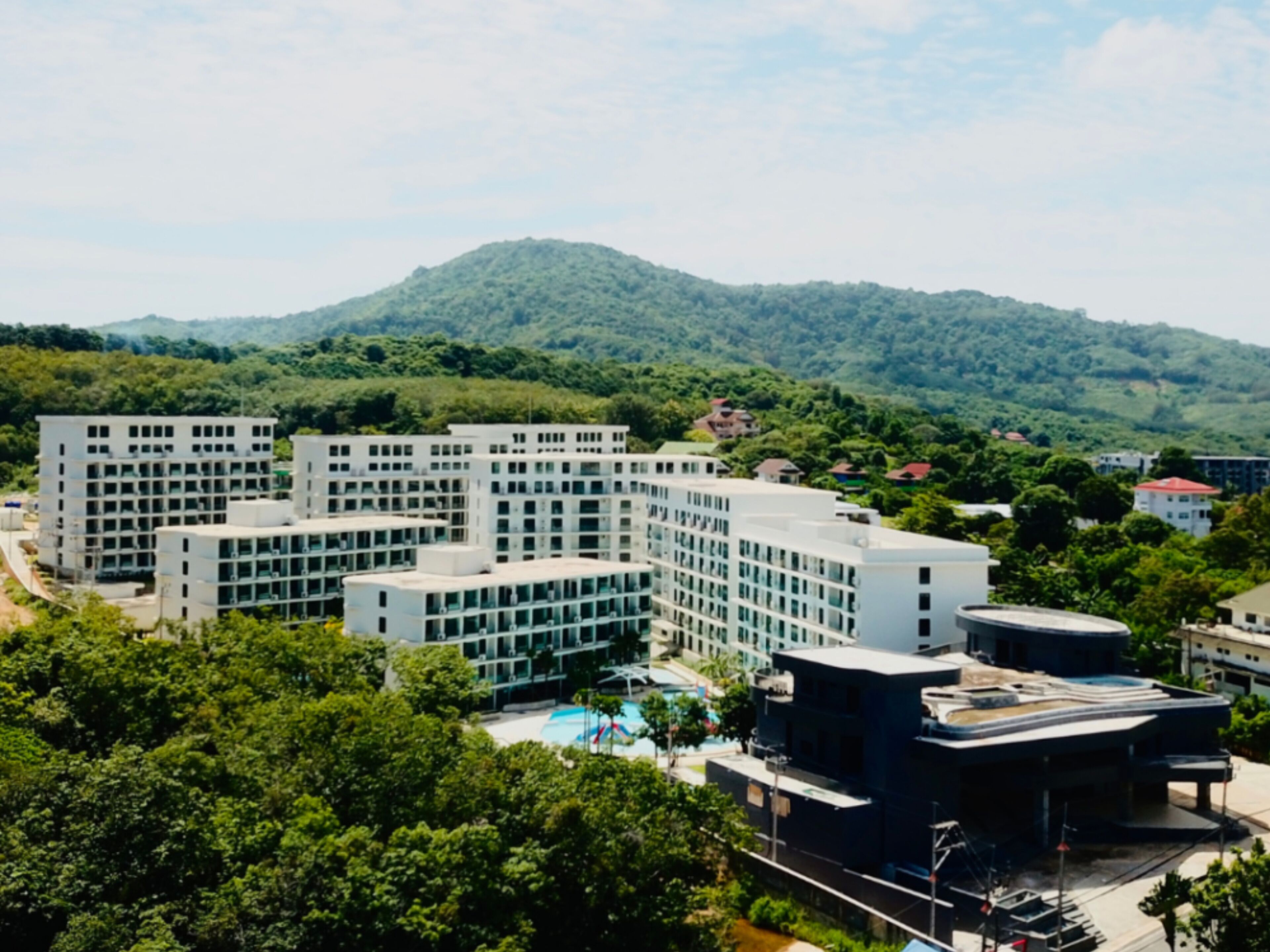 A modern hotel complex with multiple buildings, a swimming pool, and a mountainous backdrop.