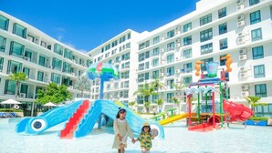 Een waterpark met glijbanen en speelconstructies, omringd door een hotel met meerdere verdiepingen en balkons.