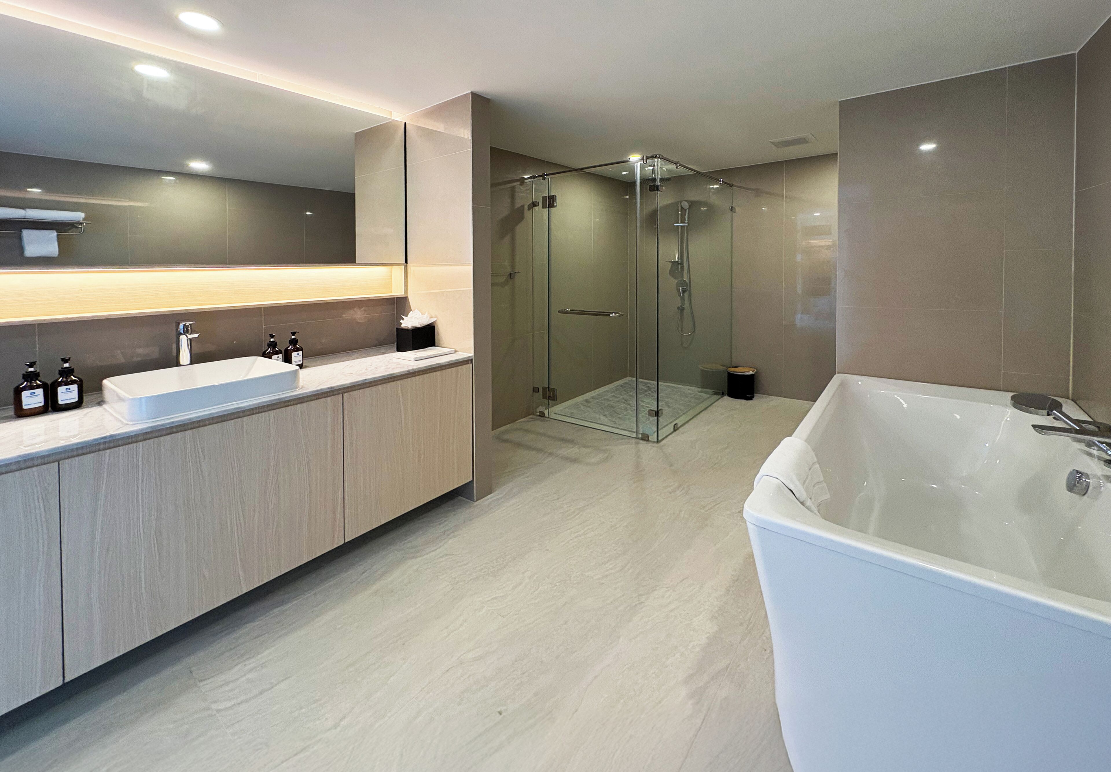 A modern bathroom with a large mirror, a bathtub, a glass-enclosed shower, and a vanity with a sink and bottles.