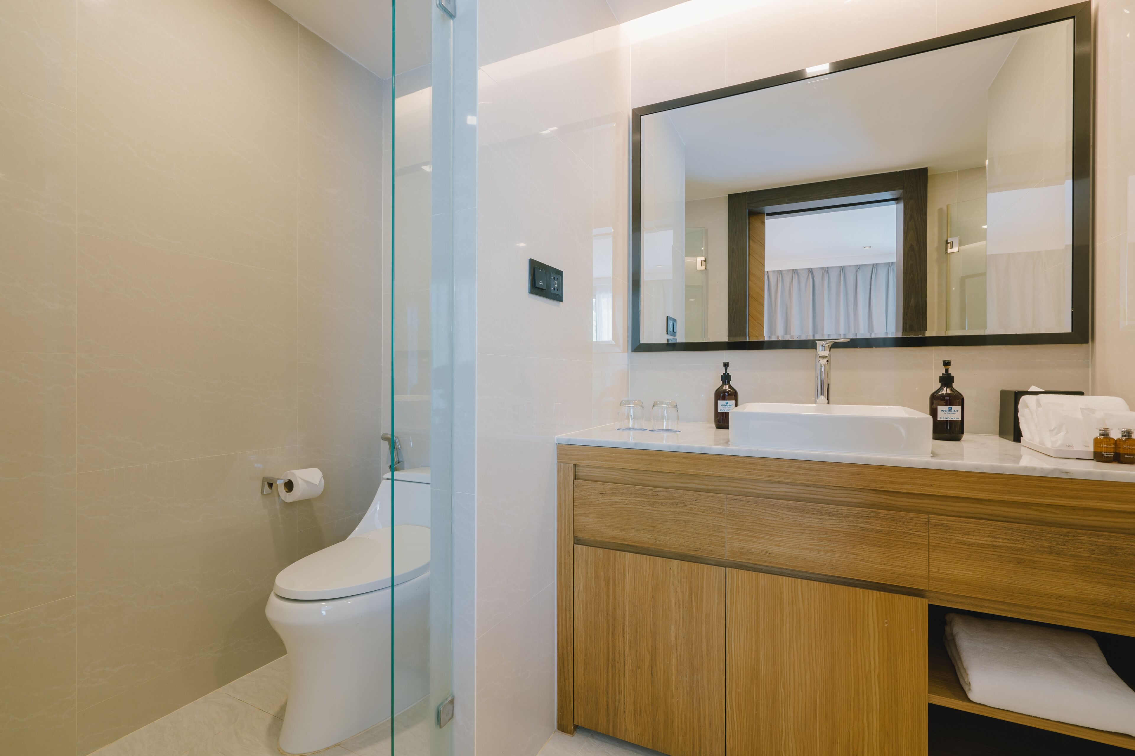 Une salle de bain moderne avec une douche à parois de verre, des toilettes blanches, un meuble-lavabo en bois avec un miroir et un évier.