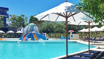A swimming pool with lounge chairs and umbrellas, a water slide, and palm trees.