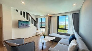 Een moderne woonkamer met een bank, fauteuil en een flatscreen televisie aan de muur.