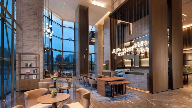 A modern hotel lobby with a central seating area, a bar, and large windows offering views. - Ramada by Wyndham Hengyang Zhengxiang (Hengyang)