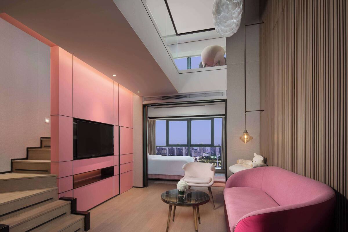 A modern living room with a pink sofa, a flat-screen TV, and a staircase.
