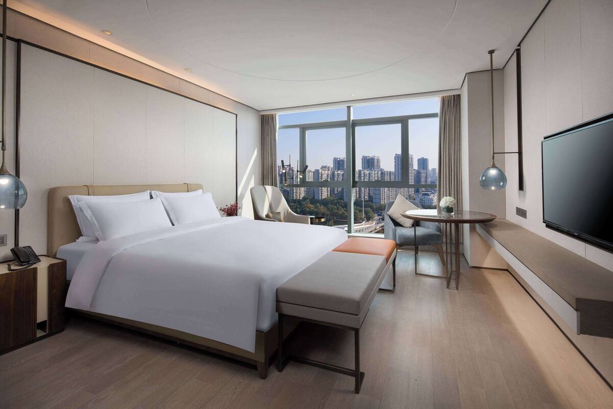 A modern hotel room with a large bed, a desk, and a TV.