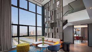 A modern living room with large windows, a sofa, a coffee table, and a dining area with chairs and a table. - Ramada by Wyndham Hengyang Zhengxiang (Hengyang)